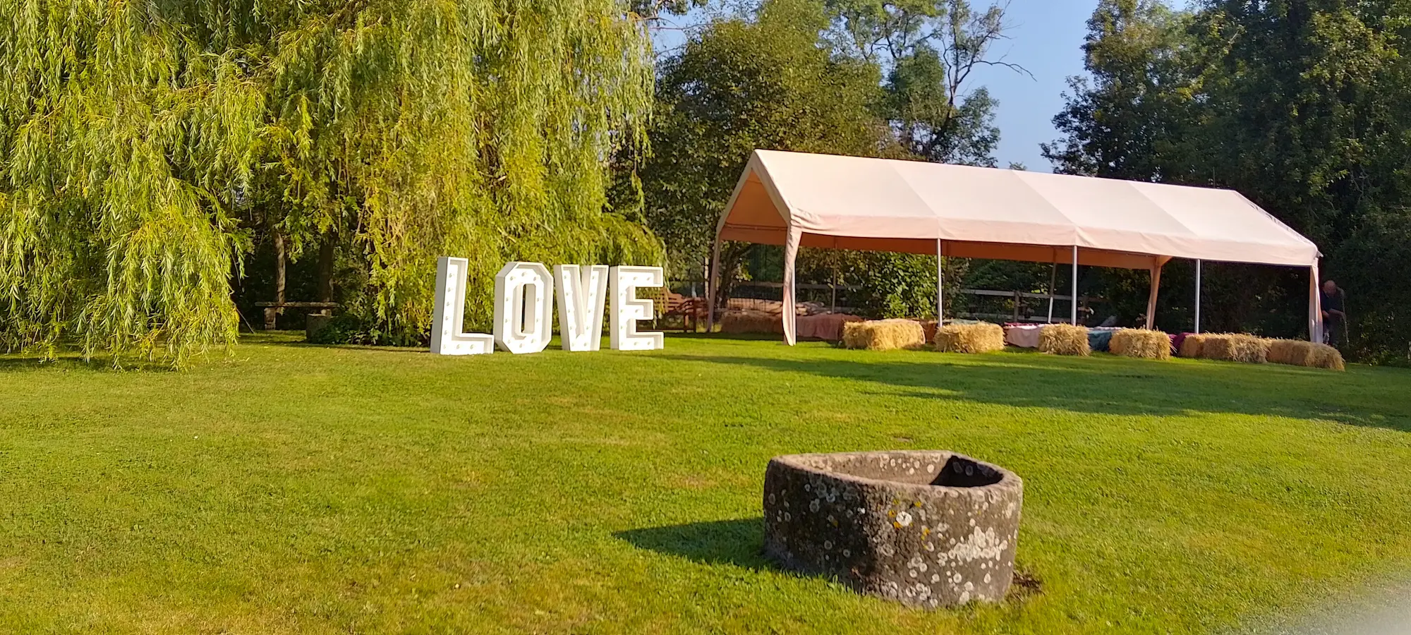 A green lawn with a stone trough in the foreground. In the background stands a gazebo and large freestanding letters that spell LOVE.